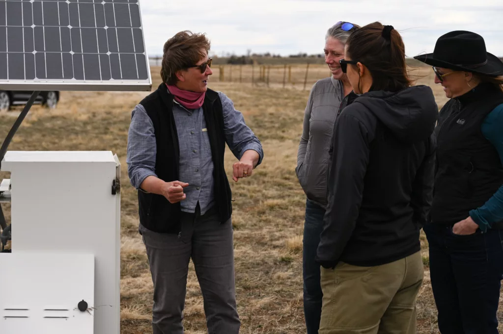 4 people talking in front of opened enclosure box with solar panels