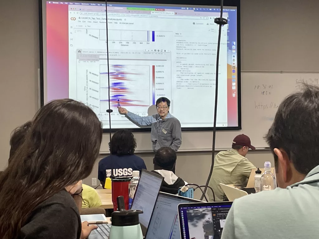 person presenting in classroom points to graph on screen