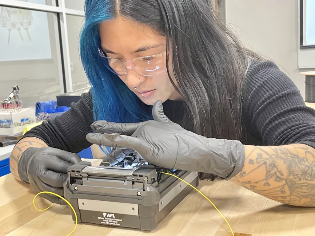 person wearing gloves carefully feeds cable into a box-shaped device