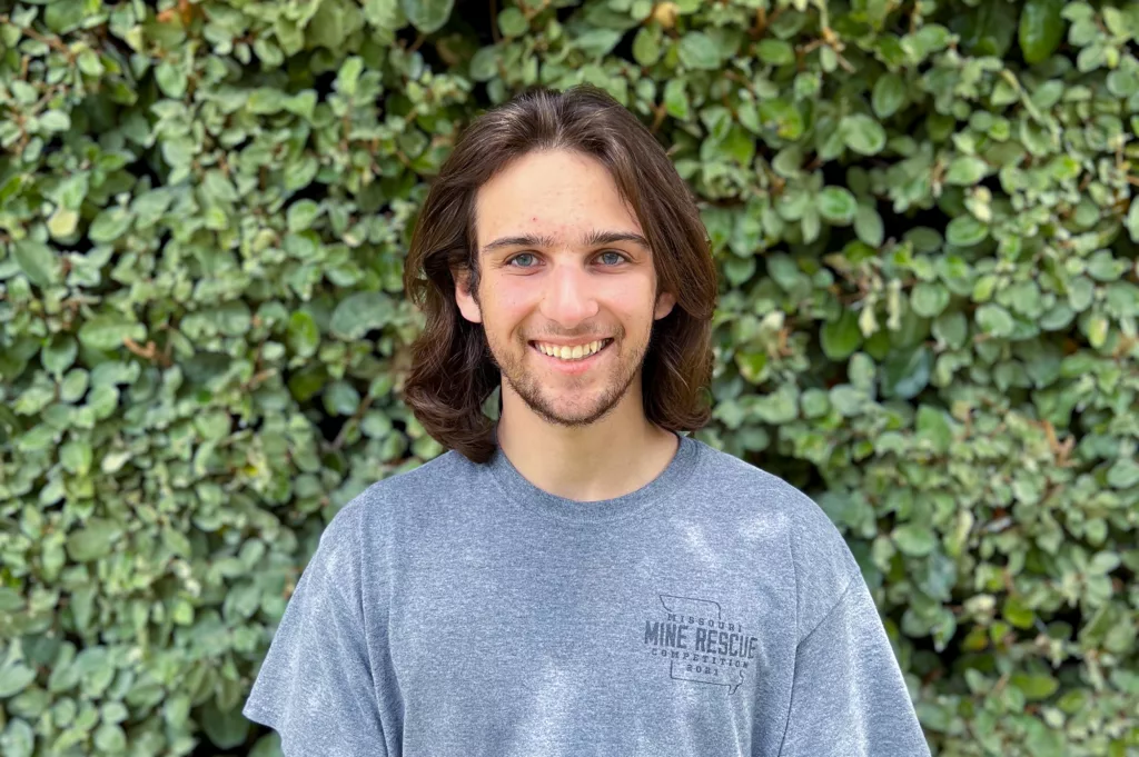 URISE intern Grant Clark smiling for a headshot with green foliage in the background.