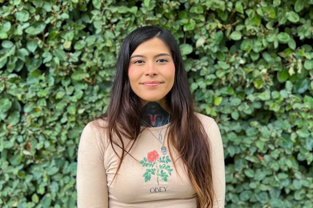 GLP intern Kaissa smiling for a headshot with green foliage in the background.
