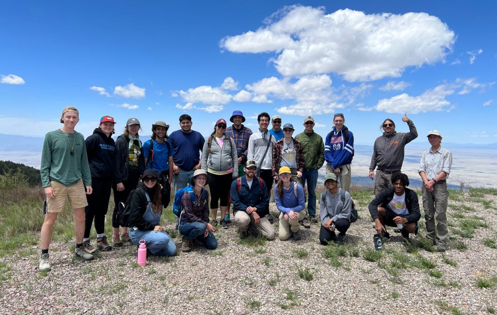 Group photo of two rows of students and instructional staff at the top of a mountain with big blue skies in the background.