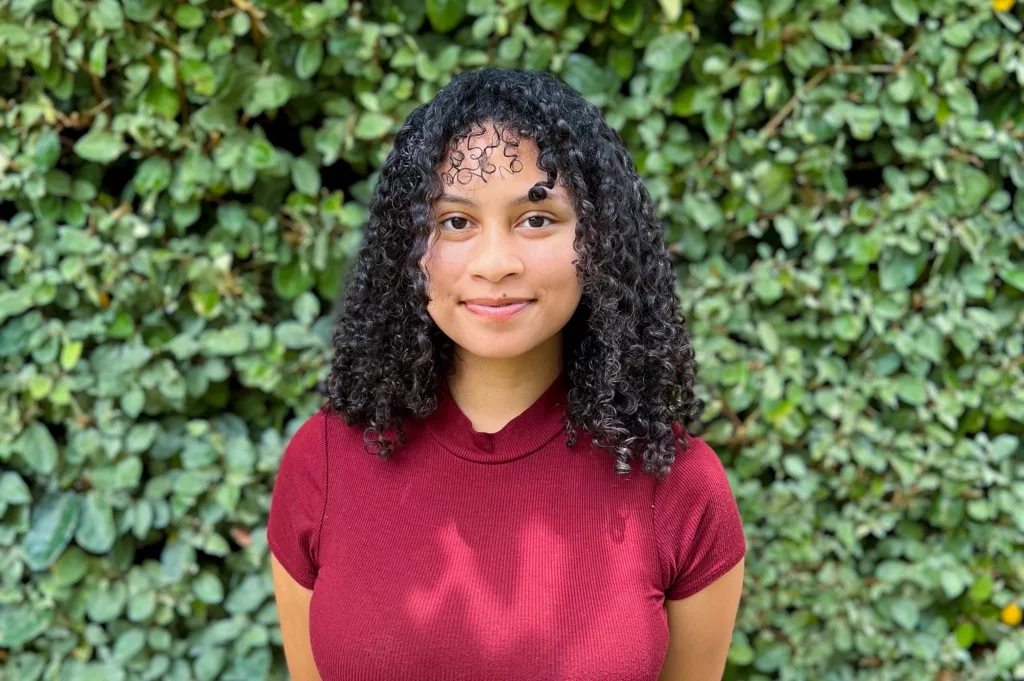 Natalie smiling for her headshot with green foliage in the background.