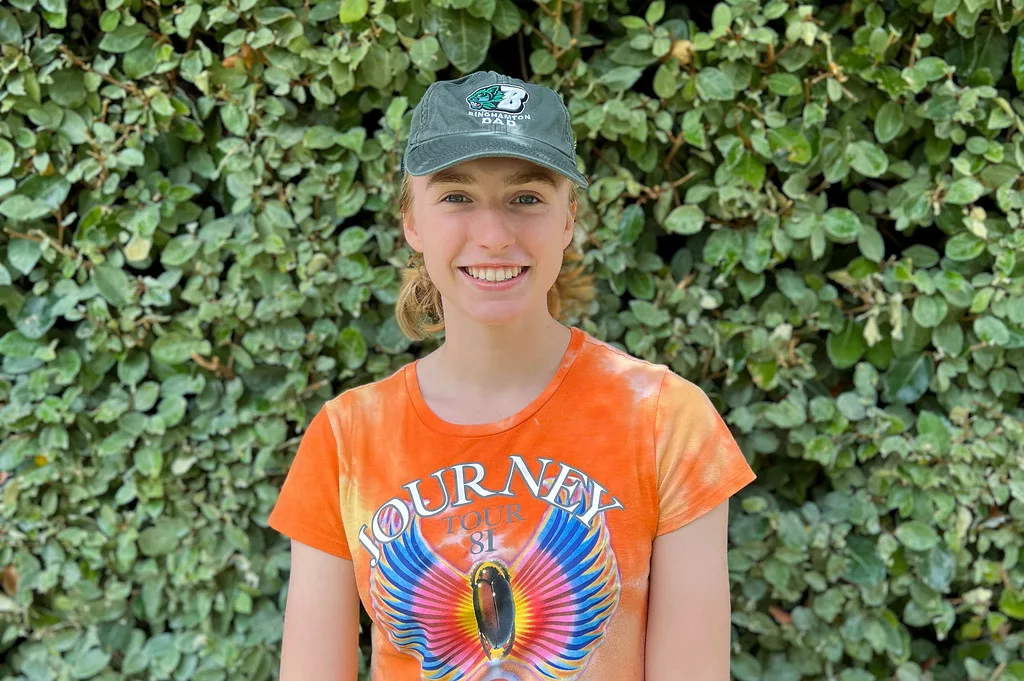 URISE intern Sarah Ayling smiling for a headshot with green foliage in the background.