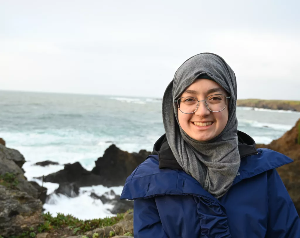 URISE intern Masooma Hasnain headshot in front of the ocean and rocks.