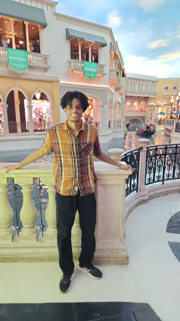 Kaetu wearing a plaid short sleeved button up standing in front of store fronts.