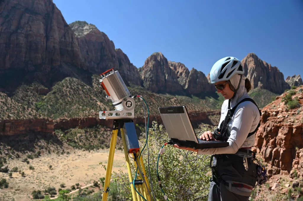 woman holds laptop operating terrestrial laser scanner on a tripod in Zion National Park