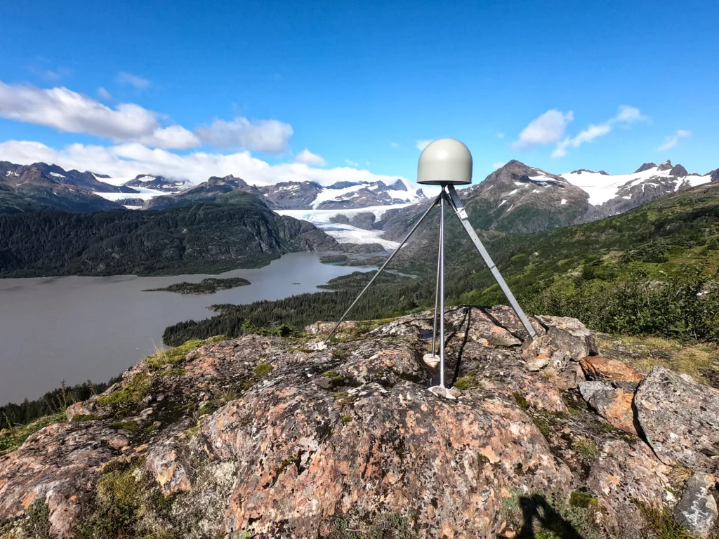 GPS antenna on bedrock outcrop in foreground, mountains and a glacier flowing into a glacial lake in the distance