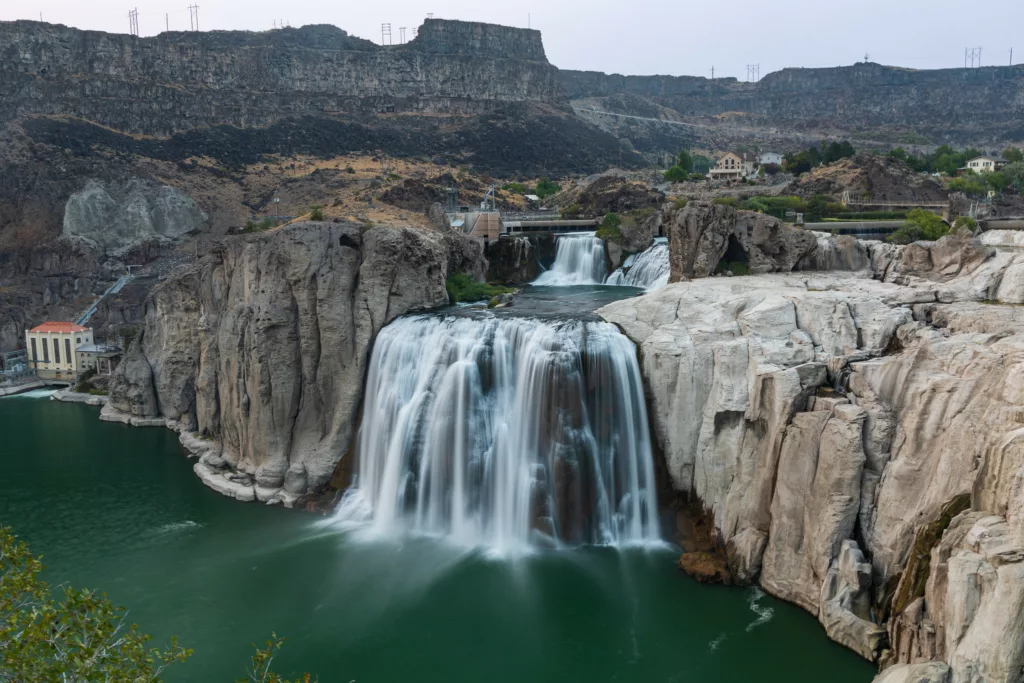 a waterfall drops over a bedrock ledge in a river valley, small dam infrastructure visible behind