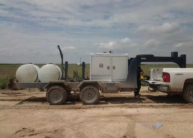 A trailer holding large drums and other equipment hooked to the back of a pickup truck