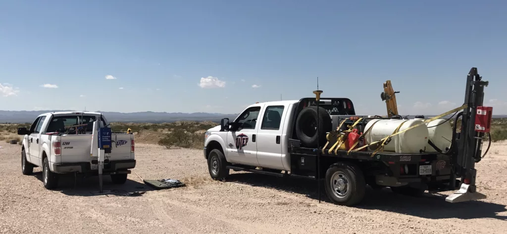 two white pick up trucks hauling gear viewed from the back