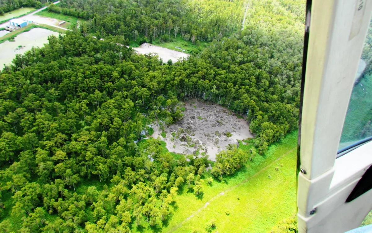 Photo taken from helicopter showing circular patch of missing trees and gray mud.