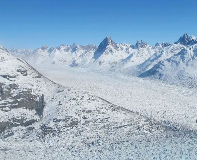 Photo looking up a glacier filling a valley, with snow-covered peaks on either side.