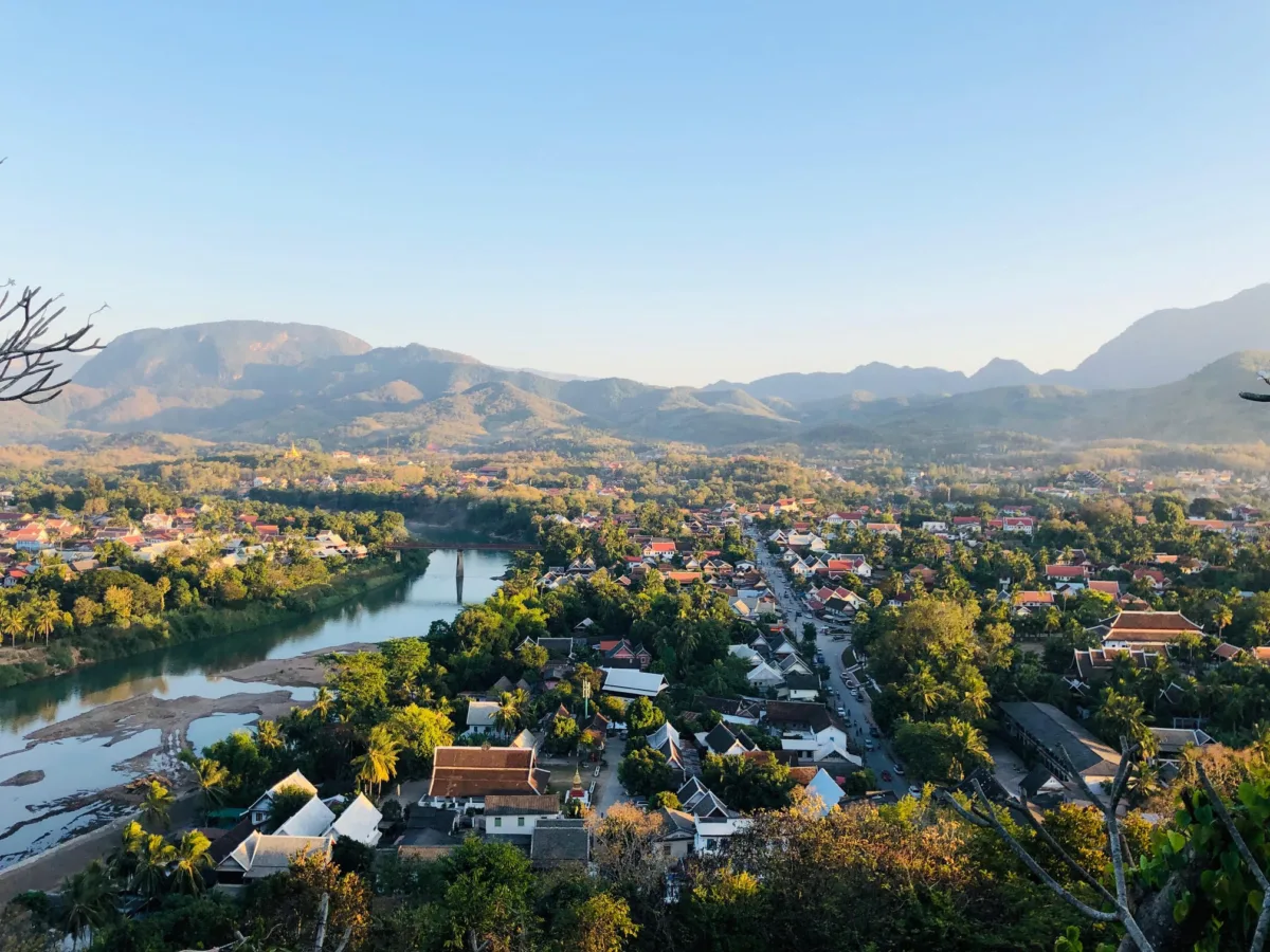 A photo overlooking a city with a river flowing through it, and green mountains in the background.