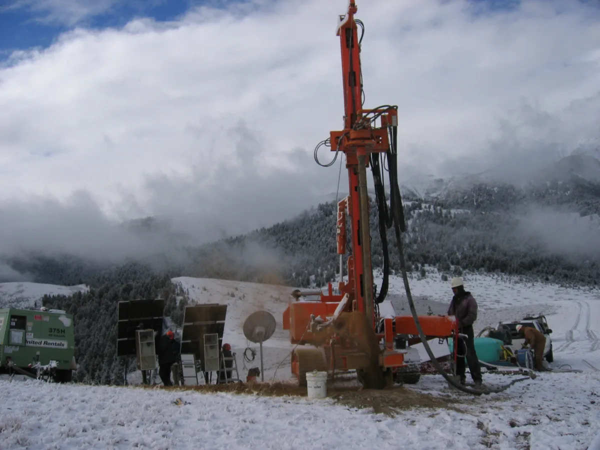 Workers surround a drill rig in a snow-covered area.