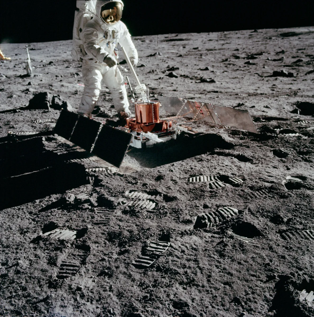 Photo of an astronaut deploying a sled-sized instrument with solar panels on either side.