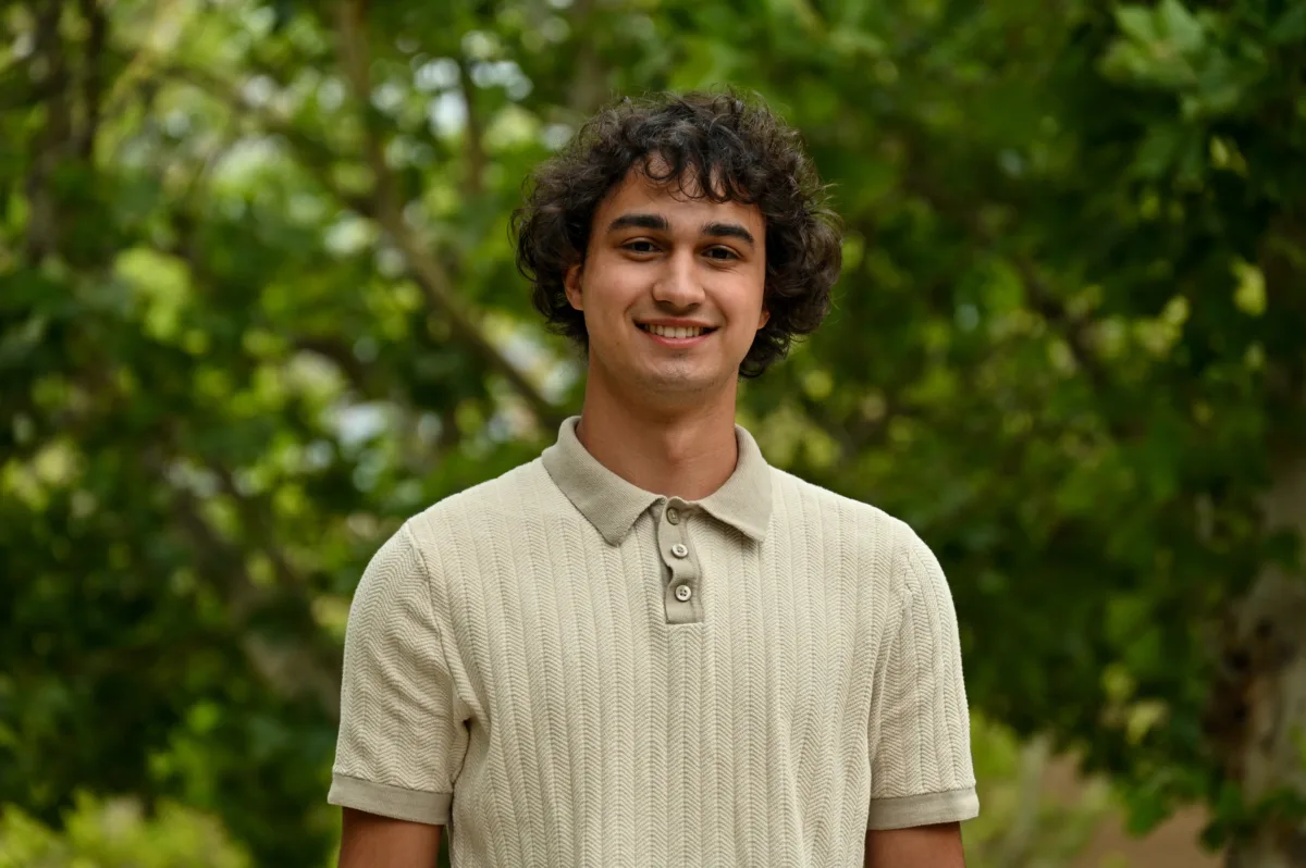 Headshot of Dylan wearing a collared short-sleeve shirt against a green foliage background