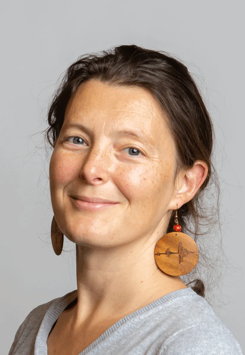 Photo of a person with brown hair tied back and circular, brown earrings.