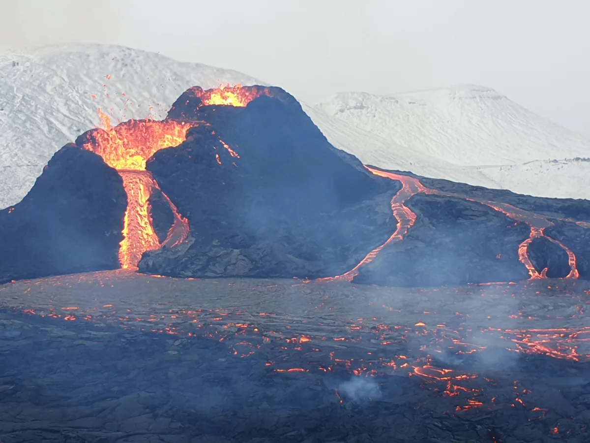 Photo of a river of lava pouring from a small cone.