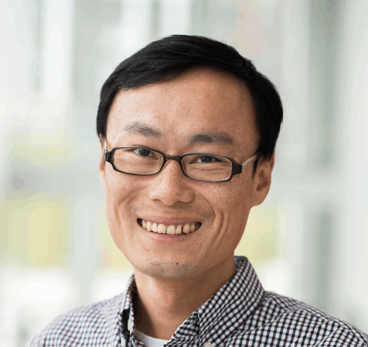 Photo of person with short dark hair and glasses wearing a print black and white collared shirt.
