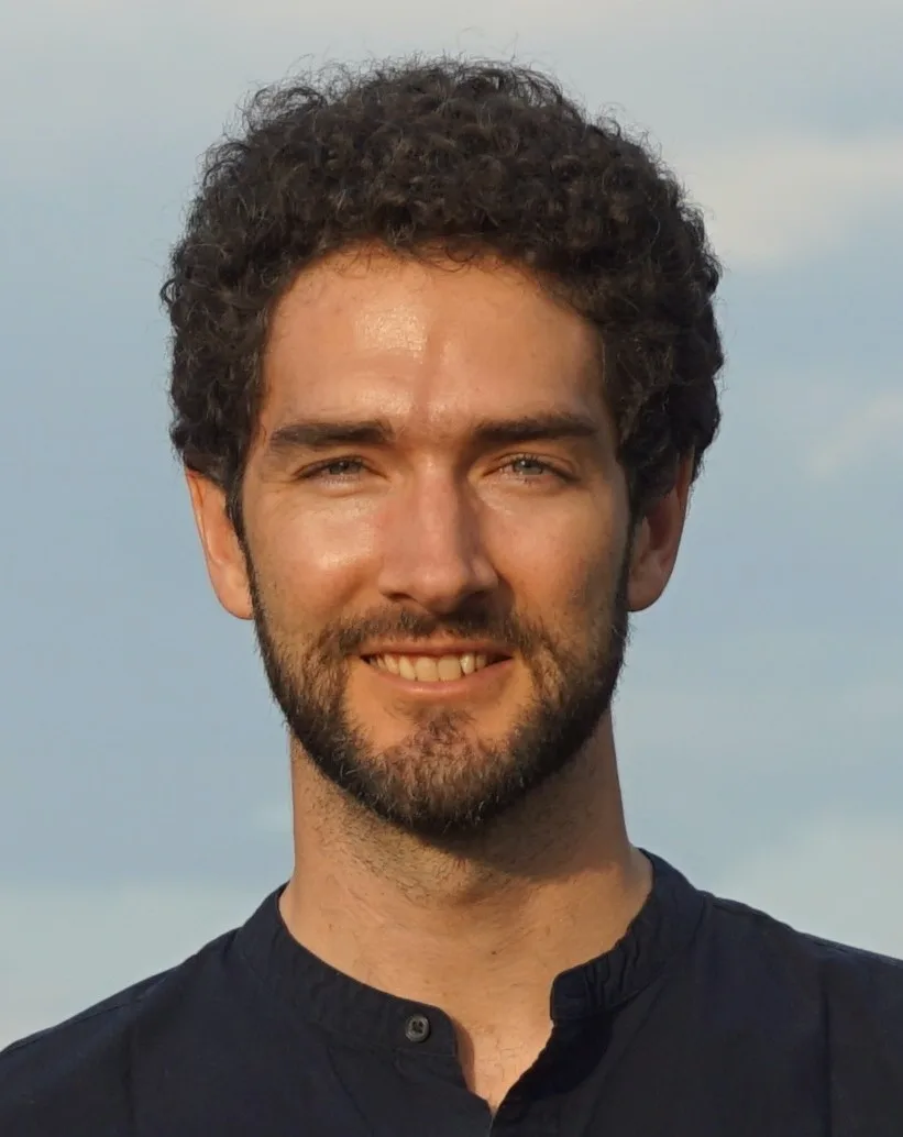 Photo of a person with short dark hair and short facial hair in a black shirt.