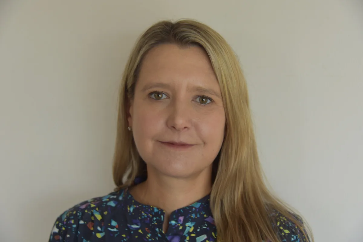 Photo of person with long blonde hair wearing a colorful print shirt.