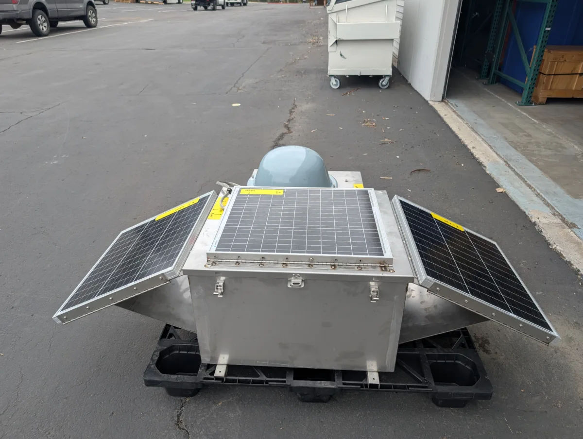 Photo of suitcase-sized steel chest with a solar panel on top and two angled off the sides like wings, and a gray plastic dome mounted on another side.