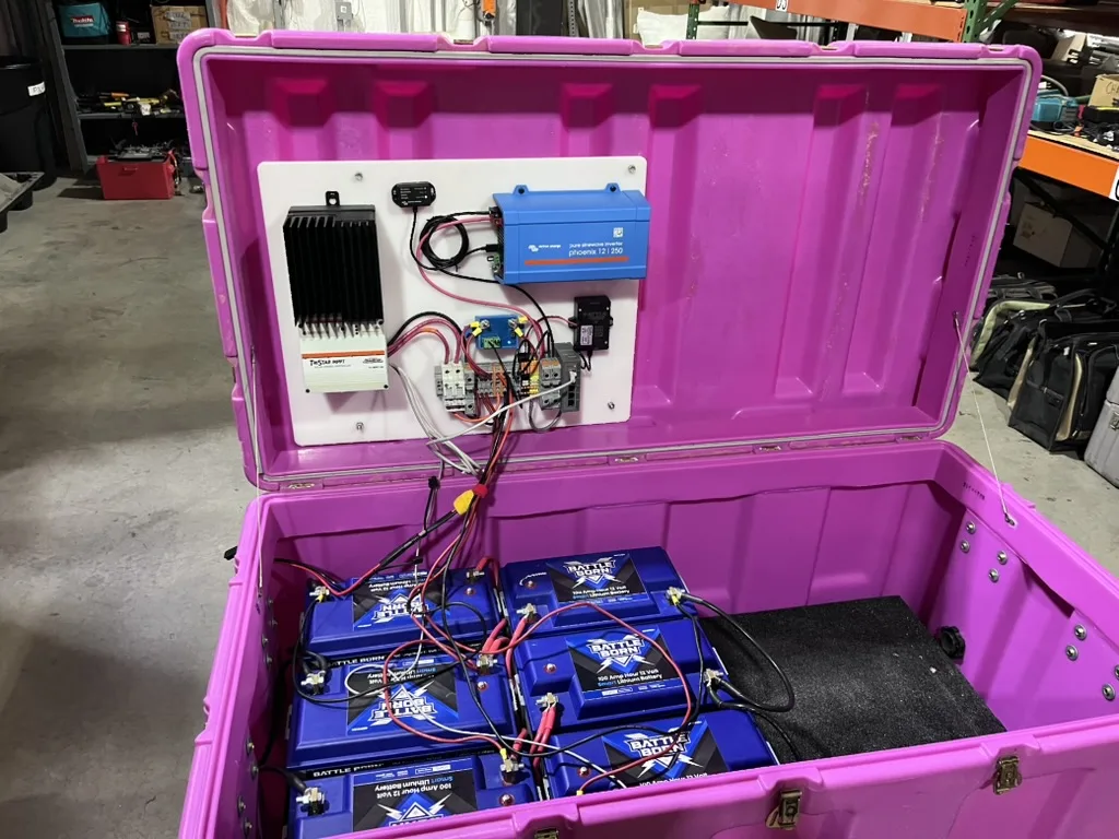 Open bright pink enclosure showing a compact DAS power system, with control electronics mounted in the lid and multiple blue batteries wired together in the base.