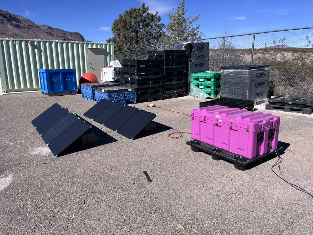 Field setup of the low-power DAS system, with foldable solar panels connected to a closed pink enclosure sitting on a pallet outdoors.