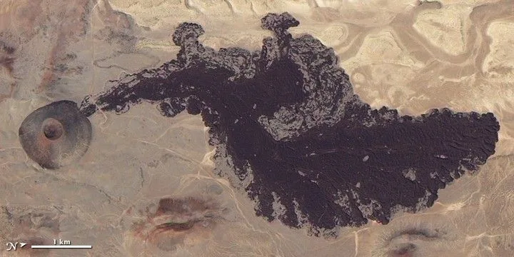 Aerial photo of a small volcano and the dark area of a lava flow extending from it.