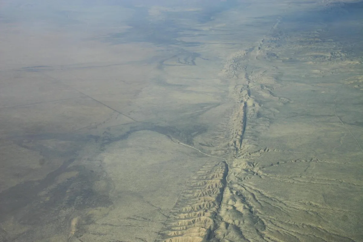 An aerial view of a fault. A linear ridge crosses the image from top to bottom and appears offset in the middle. The fault is in a brown-colored plain. 