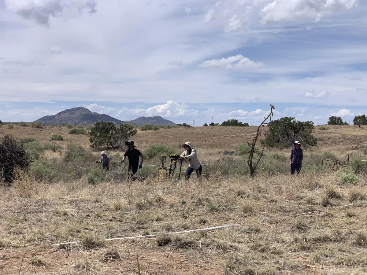Image of students pushing a GPR instrument in a grassy field dotted with trees. Desert mountains can be seen in the background.