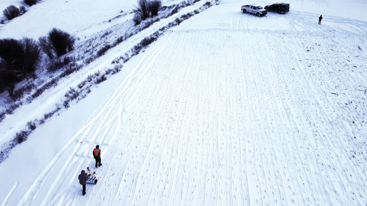 Birds-eye view of two figures completing a GPR survey on snowy ground.
